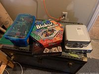 Full lot view showing container of Lego pieces, Blokus Trigon game, Scrabble game, and two metal cases.