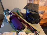 Overview of the lot showing multiple walking sticks, yoga mat, coolers, blanket, and water jugs on a folding table and floor near shelving.