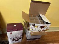 Two boxes displayed; one sealed box showing printed wine glasses, another open box with cardboard dividers holding glasses.