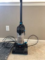 Front view of Bissell PowerForce Compact vacuum cleaner showing full unit upright on carpet with power cord loosely coiled on floor.