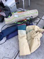 Multiple camping tents in storage bags on concrete floor including a large beige bag and several smaller colored bags.