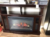 Front view of the brown electric fireplace showing the entire surround with visible flame effect inside the firebox.