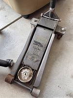 Full view of the floor jack showing the handle and wheels on the base, visible wear and rust.