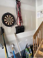 Overview of dartboards, jumper cables, shovel, and soil bags hanging in garage next to staircase