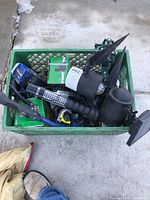 Crate with assorted gardening items including multiple black plastic yard stake lights, a garden sprayer, packaged fertilizer box and other accessories.