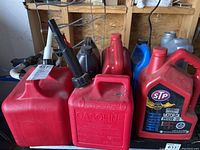 Multiple gas cans, motor oil, antifreeze/coolant containers grouped together on shelf in garage.