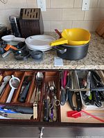 Overview of countertop and open drawers with knives, utensils, cookware, and plates.