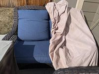 Loveseat showing blue cushions and partial coverage by beige protective cover outdoors.