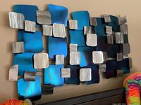 Full view of the metal wall art showing the geometric arrangement of blue-green, silver, and black metal panels.