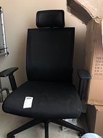Black office chair with cushioned fabric seat, mesh backrest and mesh adjustable headrest, black adjustable armrests, and wheeled base.