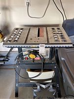 Front view of Ryobi 10 inch table saw on metal stand with some accessories below.