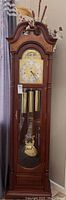 Front view of full grandfather clock with case, weights, pendulum and floral arrangement