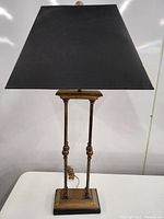 Full view of the table lamp showing the black rectangular shade, brass twin column base, square base with black trim, and finial.