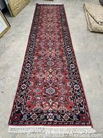 Full length top-down view of runner on floor showing red field, floral medallions, navy border and cream fringe