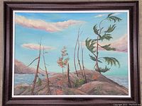 Framed oil painting showing a landscape with rocky terrain, sparse trees, water body, and a partly cloudy sky.