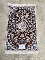 Full view of rectangular Persian carpet with floral and medallion design showing overall pattern and colors on a concrete floor.