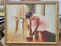 Full view of framed oil painting showing a young ballerina in pink tying her ballet shoes.