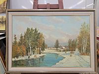 Framed signed original oil landscape painting depicting a river with snowy banks, colorful trees, and a cabin in the distance.