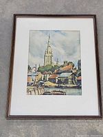 Full view of the framed watercolour painting showing a landscape of a church with a tall spire, village houses, and water with boats.