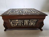 Front view of the rectangular box showing raised Chinese characters on lid and side with ornate animal-head feet