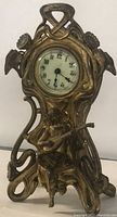 Front view of vintage bronze clock showing ornate frame, clock face, and figurine.