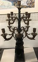 Full front view of the nine-arm bronze candelabra on display against pegboard background