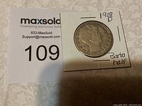 Photo of the obverse side of the 1908 D Barber Half Dollar coin in a white cardboard holder showing the date and 'Barber Half' handwritten on holder.