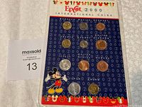Photo showing front view of EPCOT 2000 International Coins set mounted on a blue card with Mickey Mouse graphics and international coins from multiple countries.