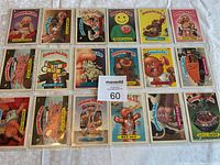 Full set of 18 Garbage Pail Kids cards arranged on a white cloth, protected in plastic sleeves, showing colorful cartoon characters and their names.