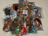 Photo showing 12 sealed McDonald's TY animal plush toys in clear plastic bags spread out for display on a patterned surface.