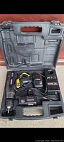 Open hard plastic case showing cordless electric drill, battery pack, charger, and cables