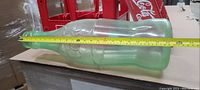 Green glass Coca-Cola bottle with measuring tape showing length near 24 inches