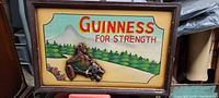 Full view of Guinness For Strength wooden plaque with colorful painted scenic background, framed in wood.