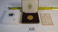 The medal displayed in its original presentation box alongside the protective clamshell case and certificate with measuring tape showing dimensions.