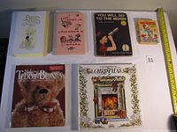Top view of six children's books arranged on a white surface with a ruler for scale, showing covers of each book including Woody Woodpecker, Best in Children's Books, Precious Moments Bible, You Will Go to the Moon, Making Teddy Bears, and A Celebration of Christmas.