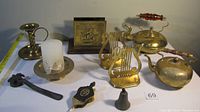 Overall shot showing the full assortment of copper and brass items arranged on a white surface against a wall including kettles, bookends, candle holders, letter holder, bell, and other items.