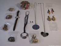 Top-down view of various costume jewelry pieces spread out on white background showing necklaces with pendants, bracelets, earrings, and wristwatch.