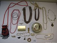 Overview of assortment of costume jewelry including necklaces, bracelets, brooches, pins, and small decorative items laid out on white cloth.