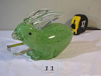 Side view of green glass bunny on white surface with measuring tape showing length approximately 8.5 inches.