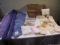 Overall view of two scarves, lace trims, and basket arranged on table, showing variety of textiles and accessories.