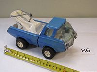 Full side view of a blue metal Tonka toy truck with white crane arm, placed next to a tape measure showing about 8.5 inches length.