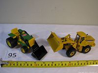 Both Tonka green tractor and John Deere yellow bulldozer displayed together with measuring tape showing approximate length.