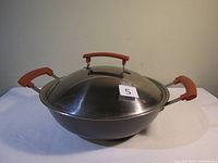 Metal wok with silicone grips on handles and lid, shown with lid on the wok.