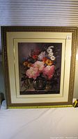 Full view of the golden ornate rectangular picture frame with a detailed floral print inside, showing various colorful flowers in a vase behind glass.