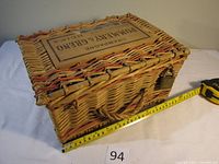 Side view of the rectangular wicker champagne box with a measuring tape indicating approximate length of 12 inches.
