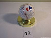 Signed Montreal Expos baseball displayed in a clear protective case with a gold-colored base, showing the official Expos logo.
