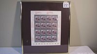 Full view of the framed sheet of stamps showing 20 stamps arranged in grid, mounted on brown mat with a thin gold frame.
