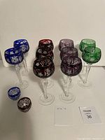 All 12 crystal glasses arranged by color showing two blue, two green, three red, three purple wine goblets and two small cut crystal glasses (one blue, one red)