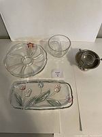 Four assorted serving pieces on white background: a Vera Wang floral glass bowl, a clear glass bowl, a sectioned glass serving plate with floral decor, and a metal bowl with glass insert for serving.