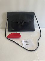 Black leather handbag with attached strap, small red leather coin holder, and MaxSold number card on a white surface.